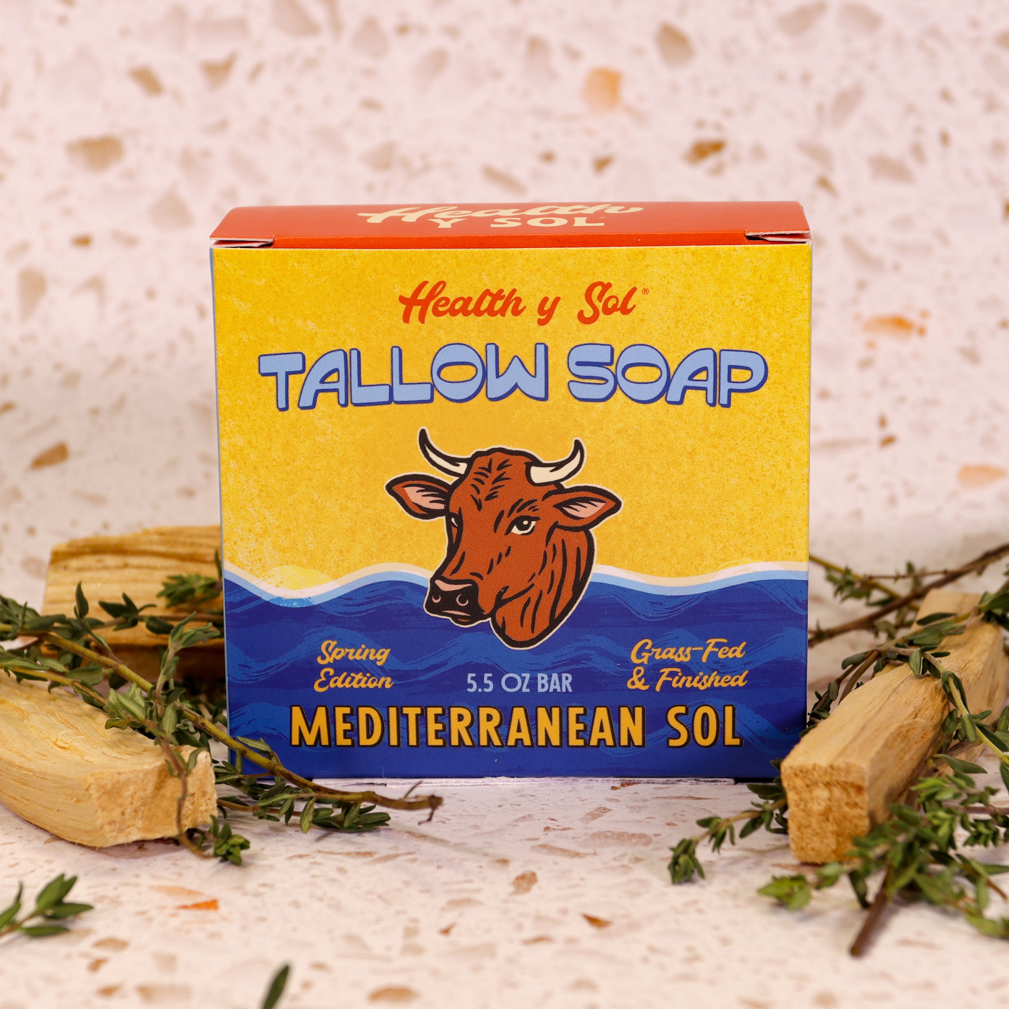Box of Health y Sol Tallow Soap with a cow illustration on a textured surface with herbs.